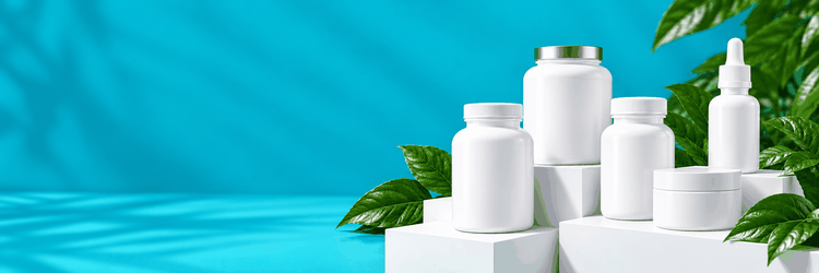 Four white supplement bottles, a dropper bottle and a small white jar on white display blocks with green leaves against a turquoise background
