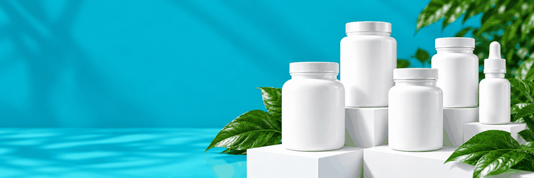 A lineup of five white supplement bottles and a white dropper bottle on white display blocks with green leaves against a turquoise background
